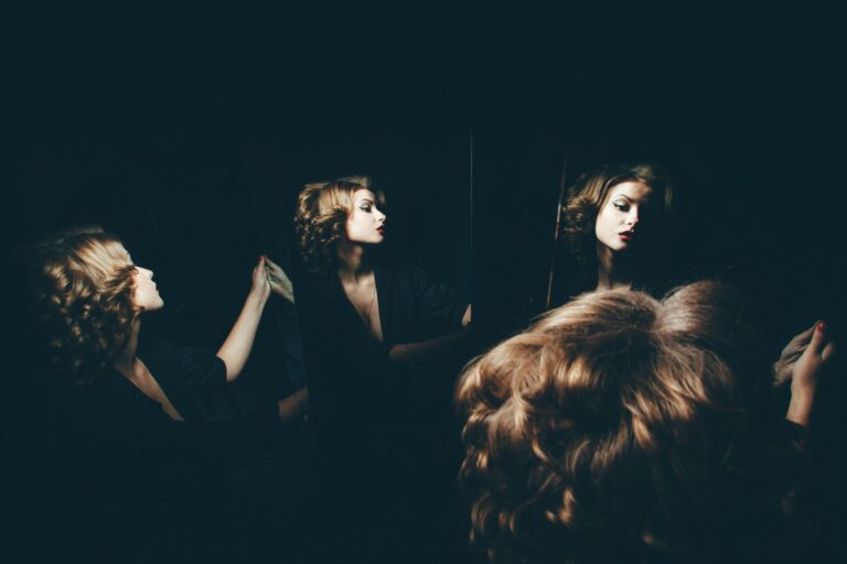 Artistic portrait of a woman reflected in mirrors, showcasing dramatic lighting and shadows.
