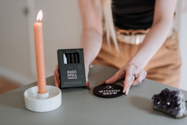 Crop anonymous female showing magic spell candles in box and witch brews on blurred background