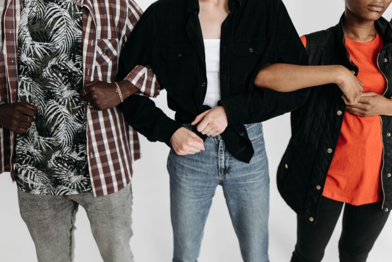 There’s No Such Thing as an Outcast Close-up of three diverse individuals linking arms, showcasing unity and connection in a studio setting.